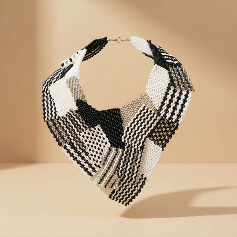 Product shot of the Beaded Collar Necklace in a black, white and gold patchwork beaded design with metal clasp, on a tan background.