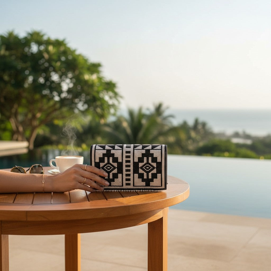 Tinkers black and white abstract beaded clutch with geometric patterns, resting on a wooden table by an infinity pool.