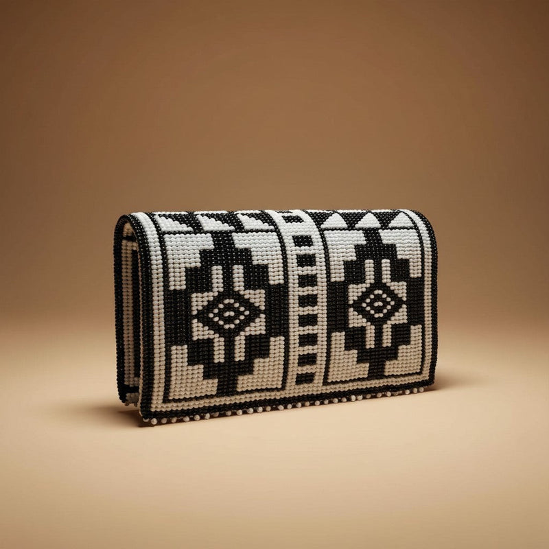 Tinkers black and white beaded clutch with abstract geometric patterns and structured rigid base on beige background.
