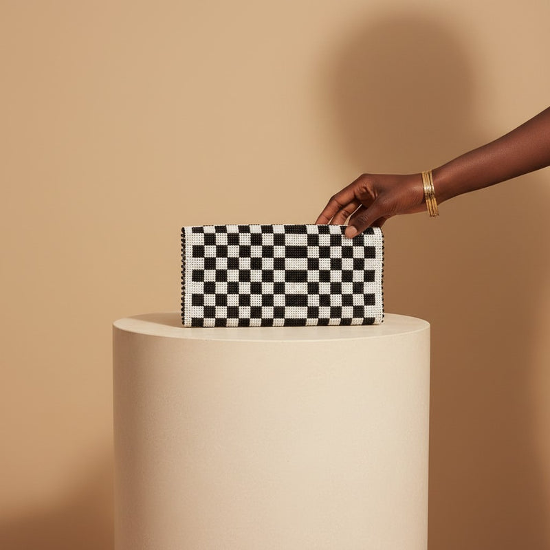 Tinkers black and white checkerboard beaded clutch held by a hand on a beige pedestal.