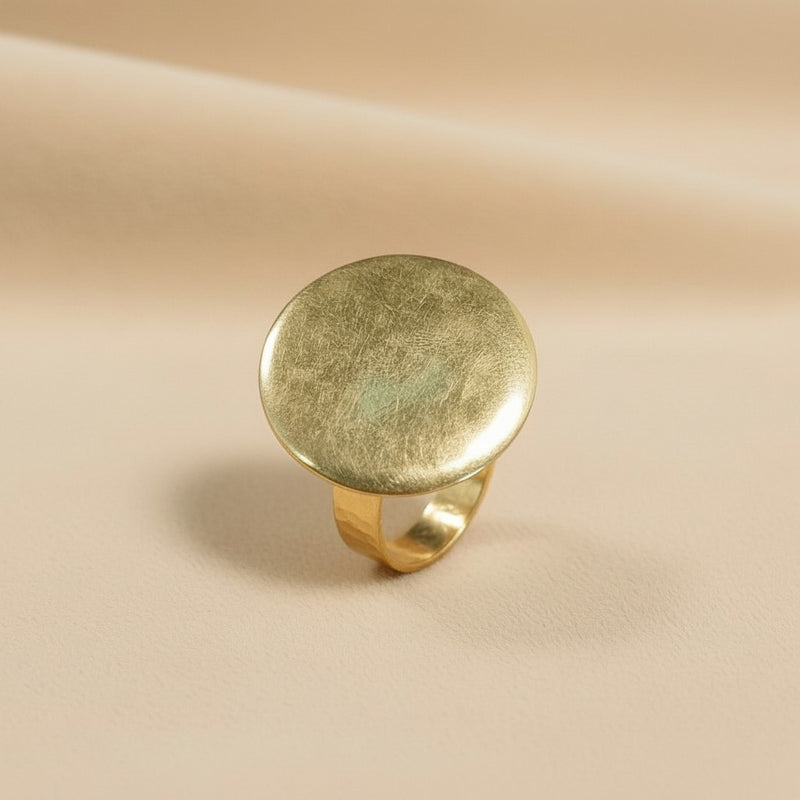 Tinkers brushed gold-tone medallion ring with a circular face on a neutral beige background.