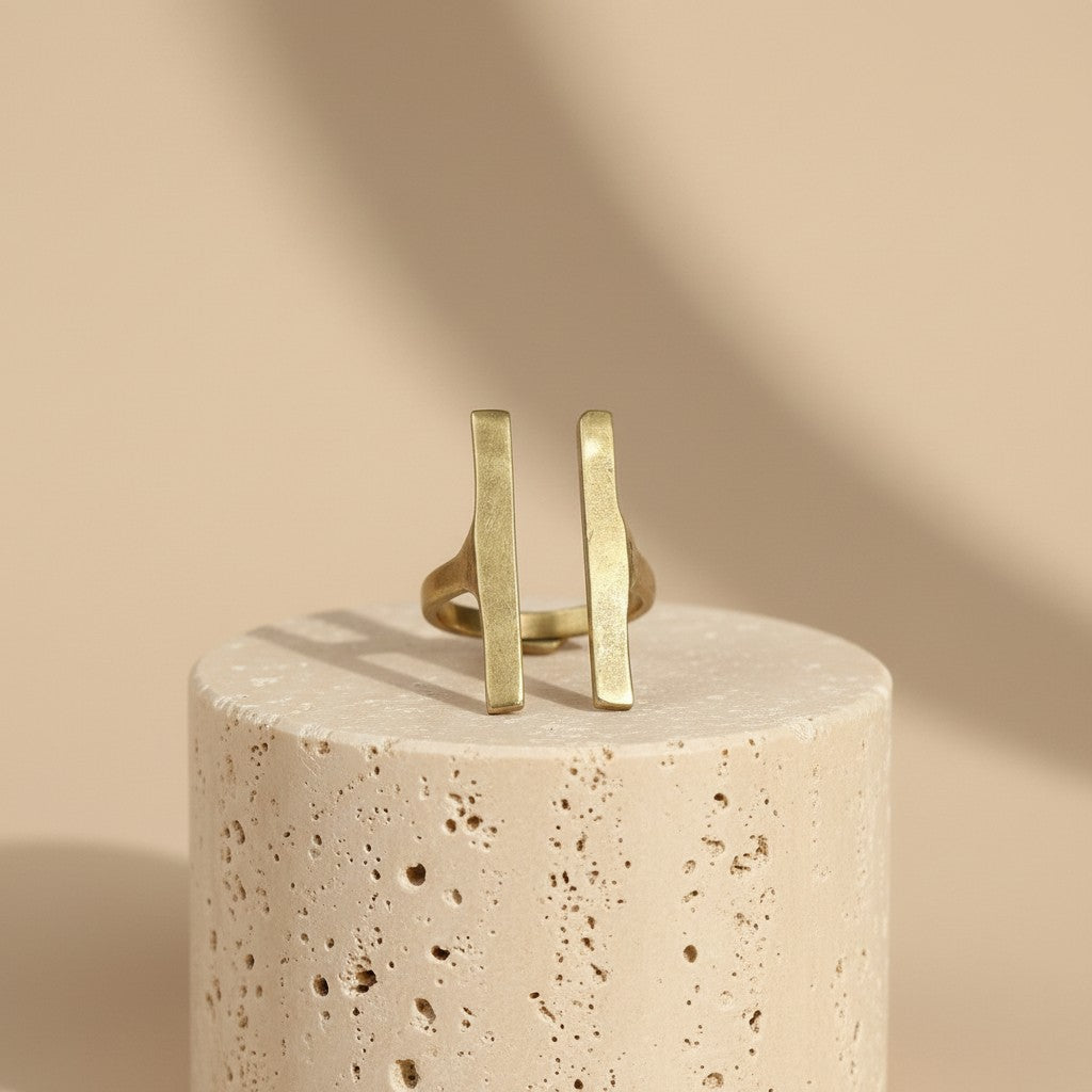 Tinkers double bar architectural brass ring with a matte brushed finish on a textured stone pedestal.