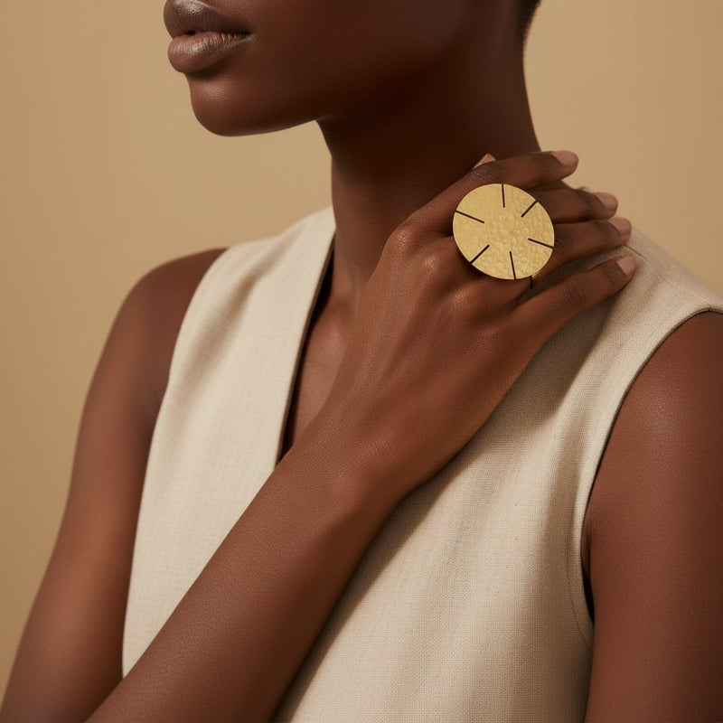 Tinkers oversized hammered brass disc statement ring with sun-ray cuts worn on a model's hand