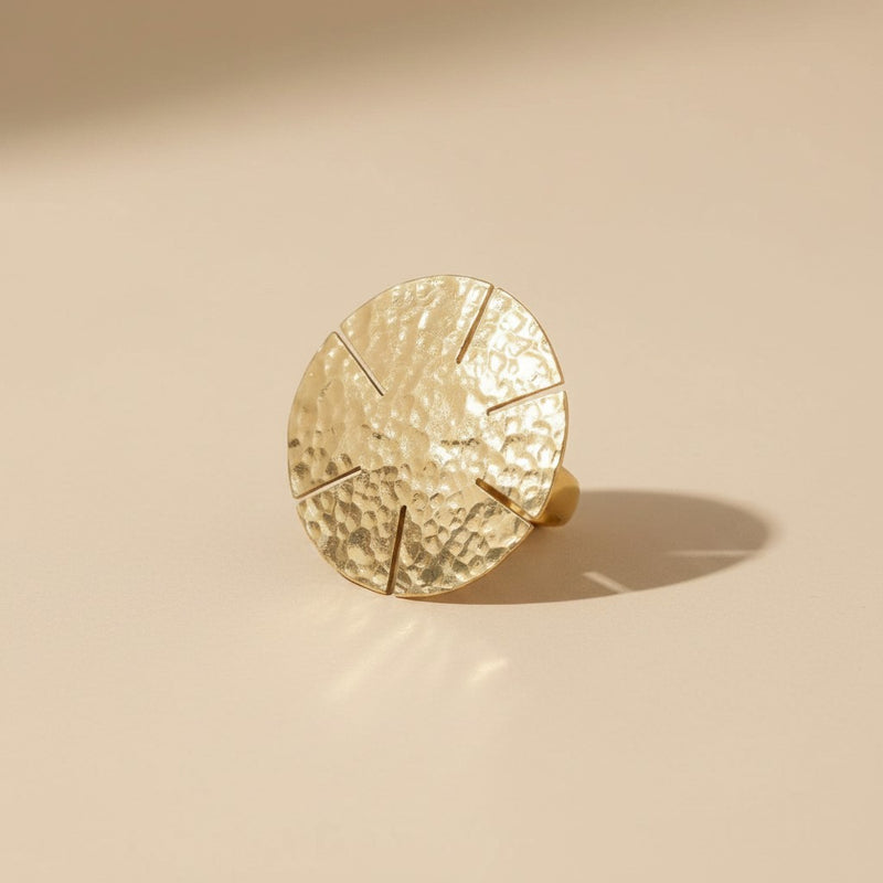 Tinkers hammered brass statement ring featuring a large sun-ray disc with geometric cuts on a textured surface.