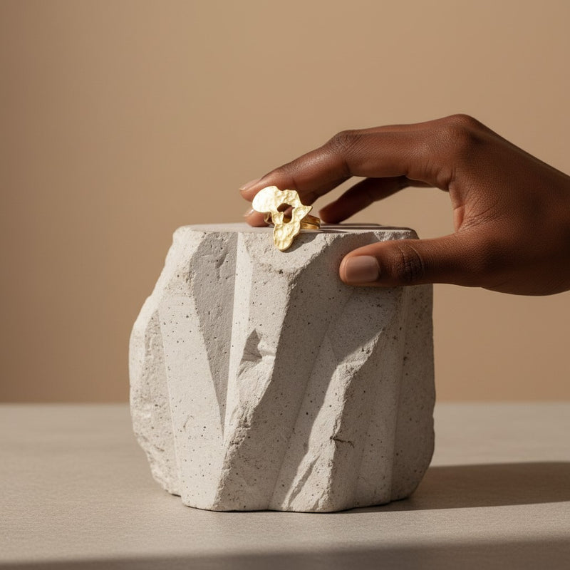 Tinkers oversized brushed brass dome ring on a textured stone block with a hand resting nearby.