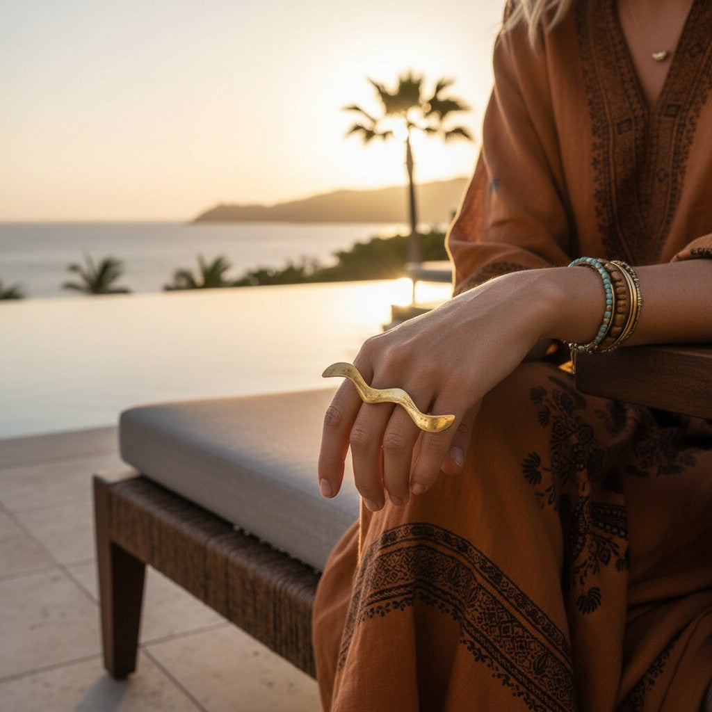 Tinkers handmade wavy brass wrap ring with a brushed matte finish worn on a woman's finger at sunset by the pool.